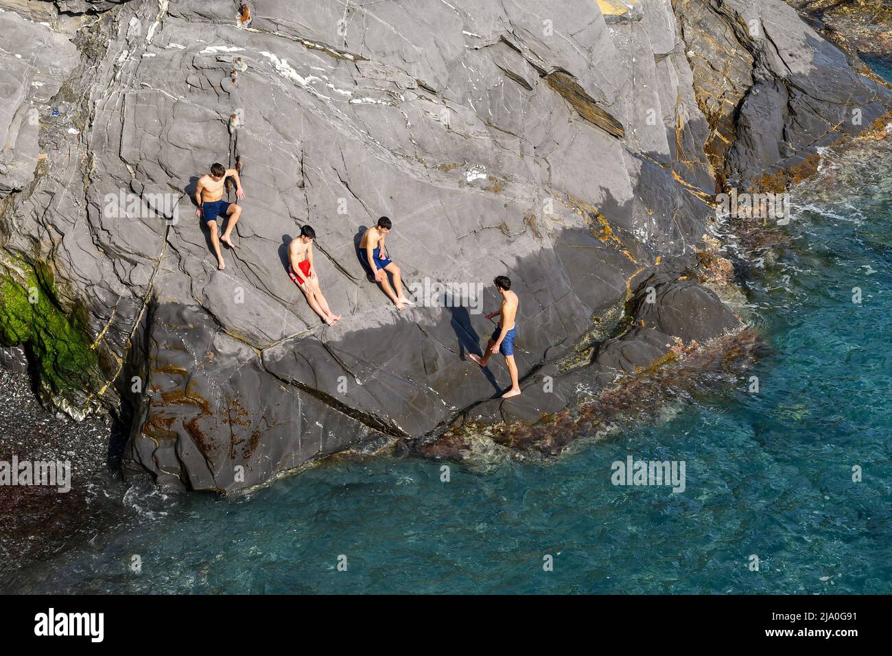 Elevated view of a cliff of the Nervi Promenade with a small group of teenagers (about 16-17 years old) sunbathing on the shore, Genoa, Liguria, Italy Stock Photo