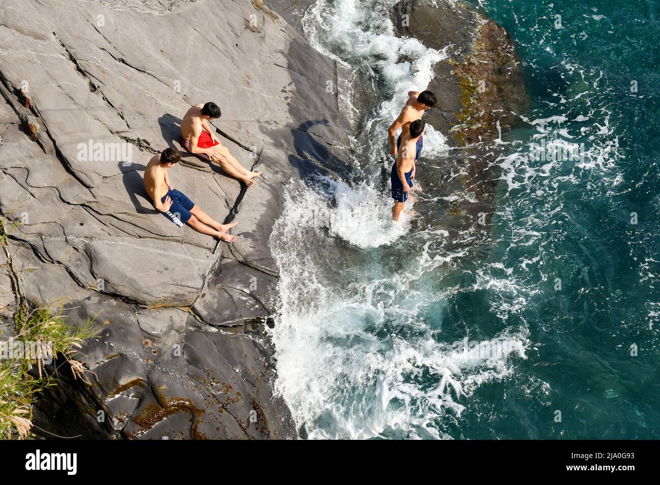 Elevated view of a cliff of the Nervi Promenade with a small group of teenagers (about 16-17 years old) sunbathing on the shore, Genoa, Liguria, Italy Stock Photo