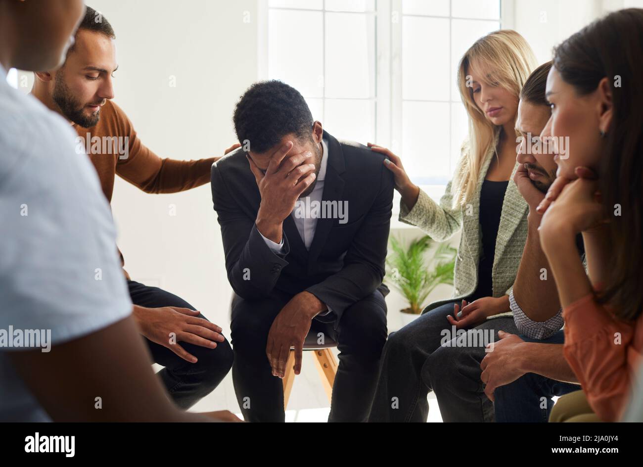 Caring people support stressed male friend at group session Stock Photo