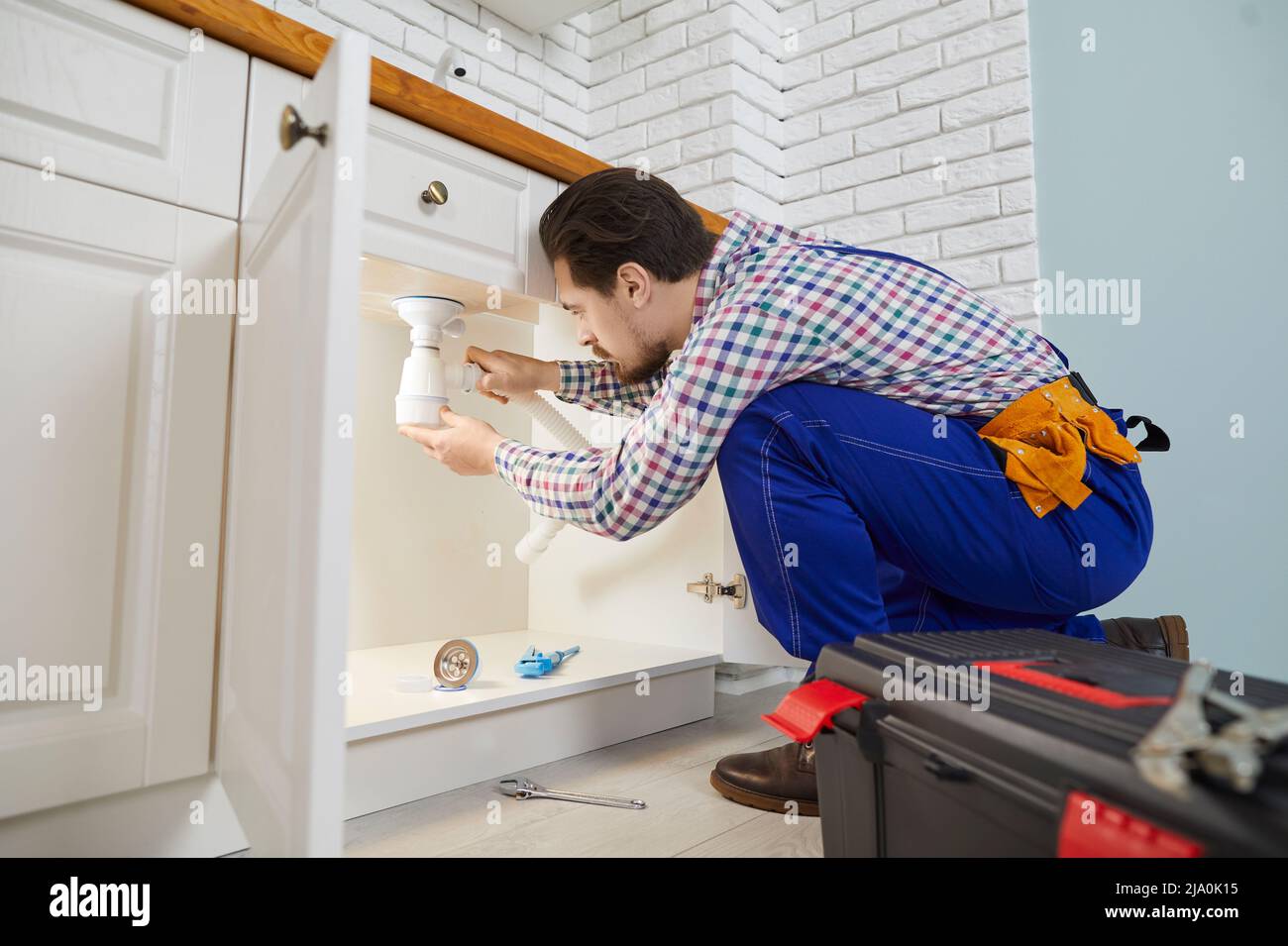 Skilled male worker plumbing repair service installs siphon under sink