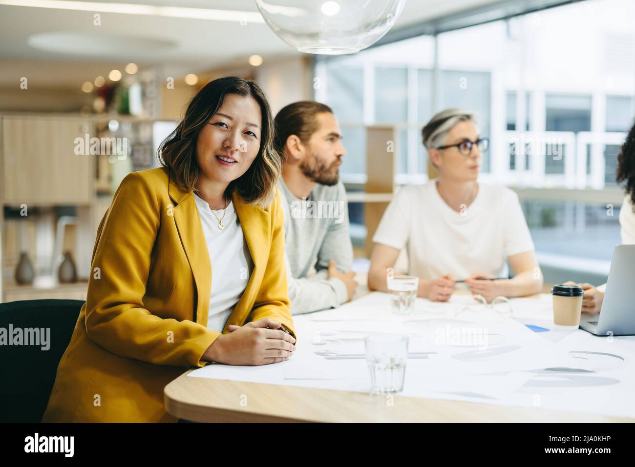 Cheerful businesswoman looking at the camera while sitting in a meeting with her colleagues. Group of innovative design professionals sharing creative Stock Photo
