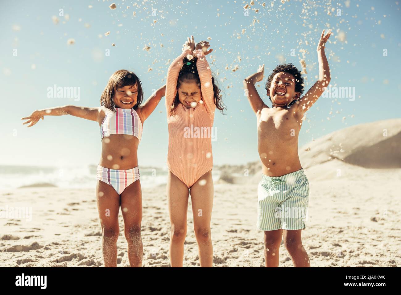 Adorable little kids having fun while throwing beach sand into the air. Group of three happy young children enjoying their summer vacation at a sunny Stock Photo