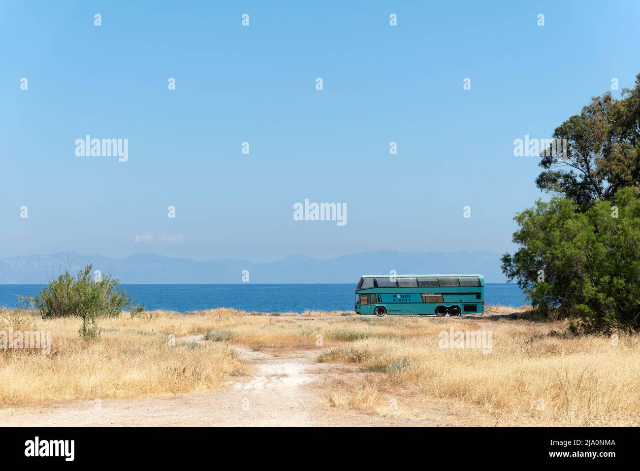 A passenger coach or bus stopped  on a a dirt road at the back of some scrub land on the edge of the Aegean Sea in Rhodes, Greece Stock Photo