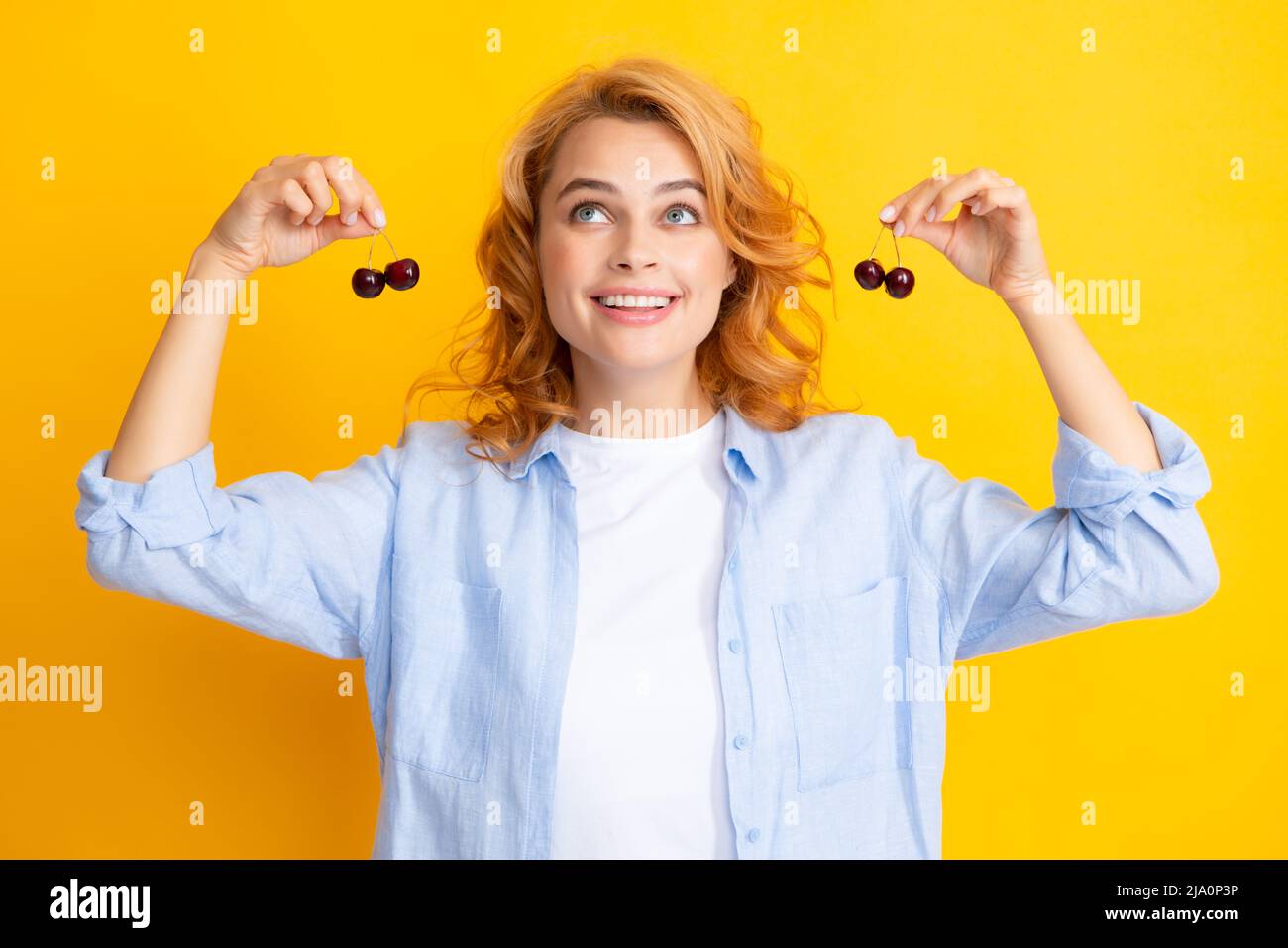 Attractive young woman eating fresh cherry. Healthy summer fruits. Yellow background. Beautiful woman posing with a cherry, girl with cherry promoting Stock Photo