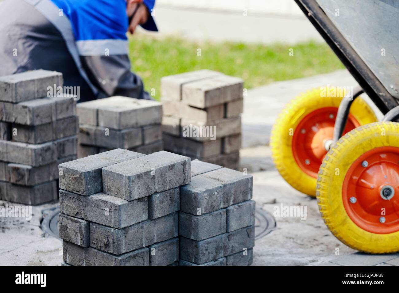 Bricklayer in work clothes sits on sidewalk and lays out paving slabs. Sight of working man in open air. Professional builder makes arrangement of territory summer day. Real scene. Stock Photo