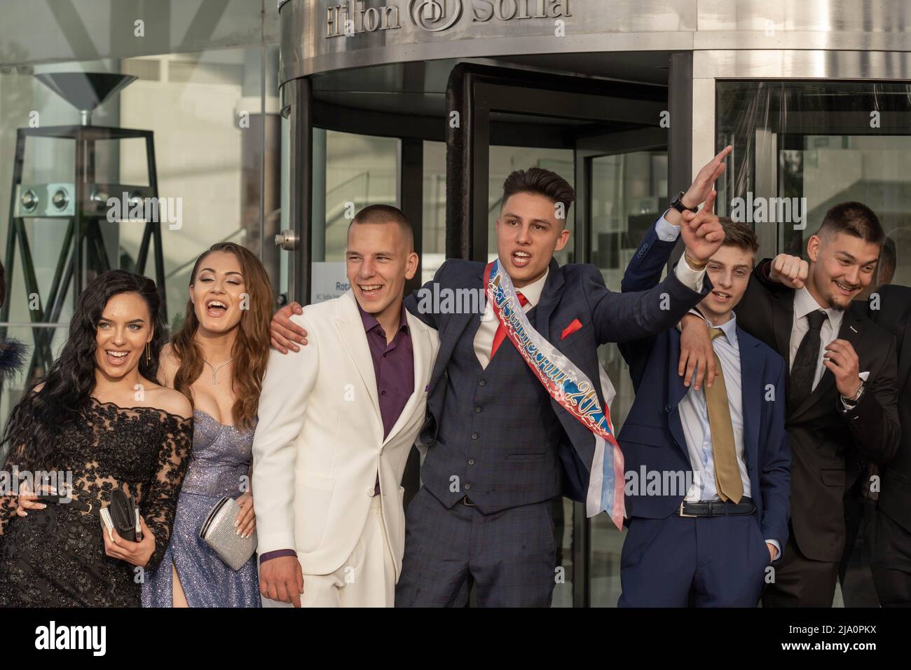 Sofia, Bulgaria - 24.05.2022, A group of students in fancy dresses enjoys emotionally the celepration of the graduate prom near the entrance of a rest Stock Photo