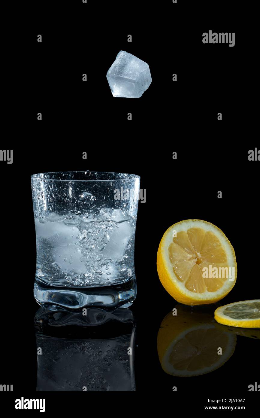 Ice cubes falling into a cocktail glass with lemon slice and ...