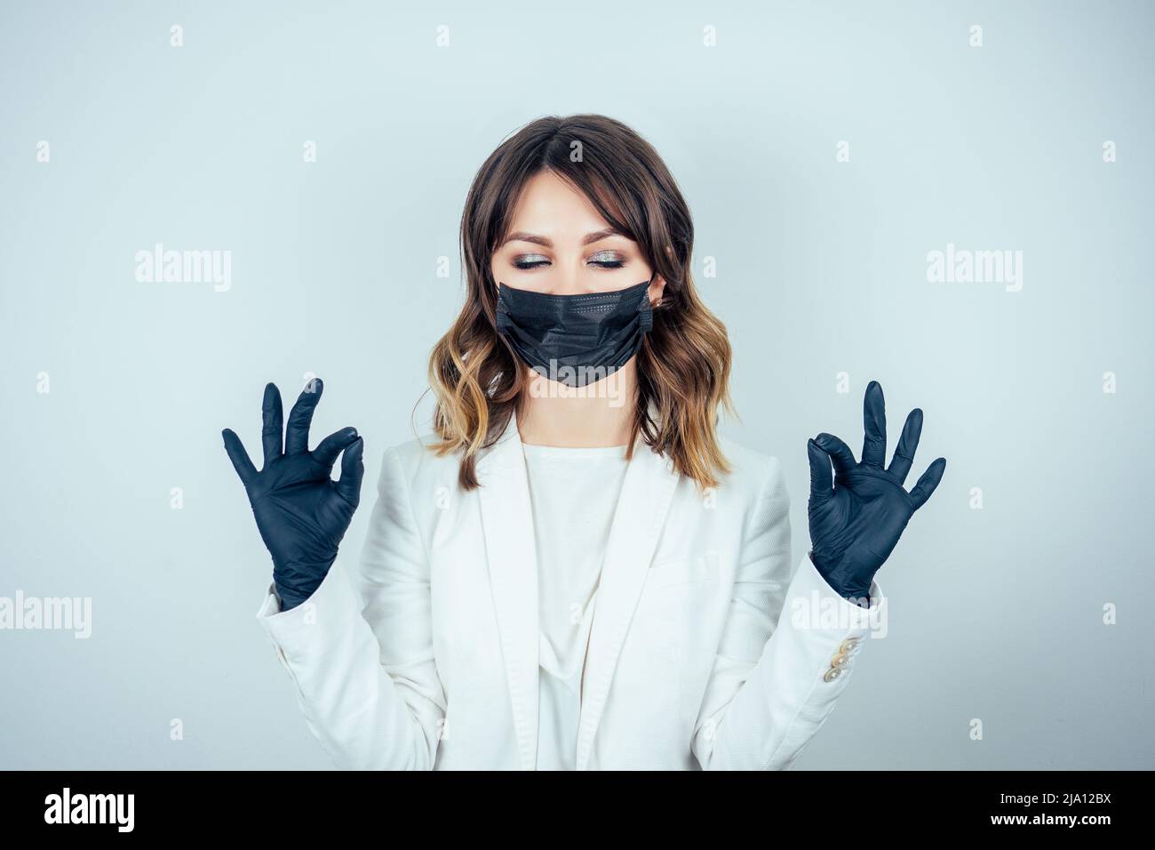 portrait of a beautiful and young doctor woman in white medical gown , black rubber gloves and black mask on face meditates and practices yoga on a Stock Photo