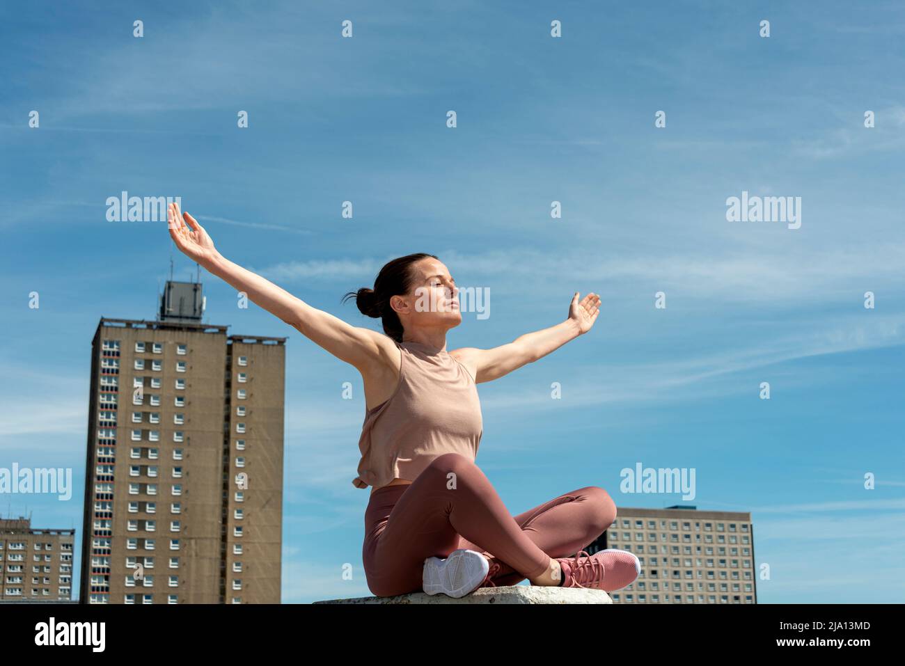 Sporty fit woman sitting crossed legged with arms outstretched enjoying the sun, Stock Photo