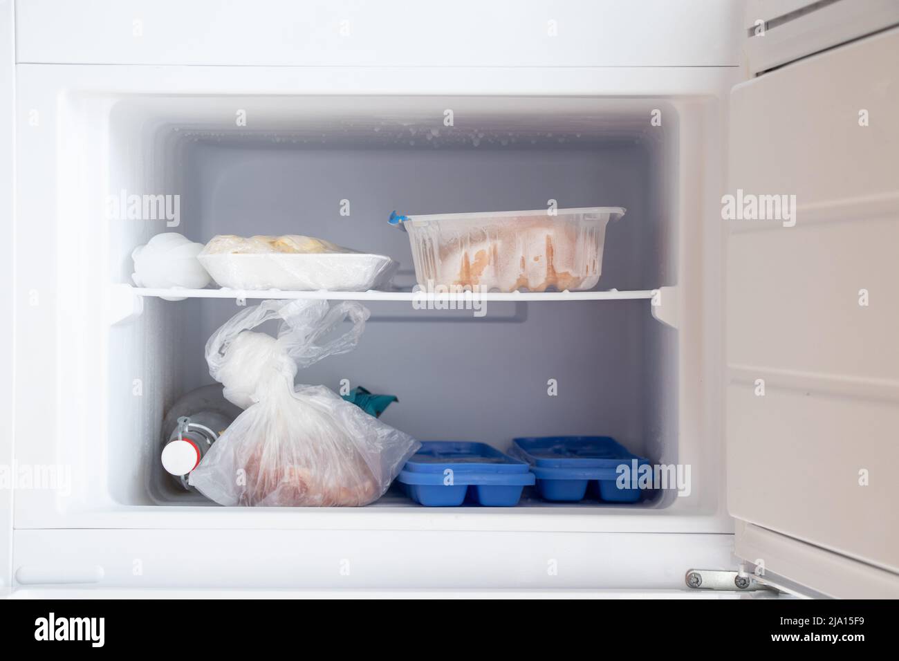 Freezer in the refrigerator, inside a tray with ice and meat and a bottle of vodka, food in the freezer in the kitchen at home Stock Photo