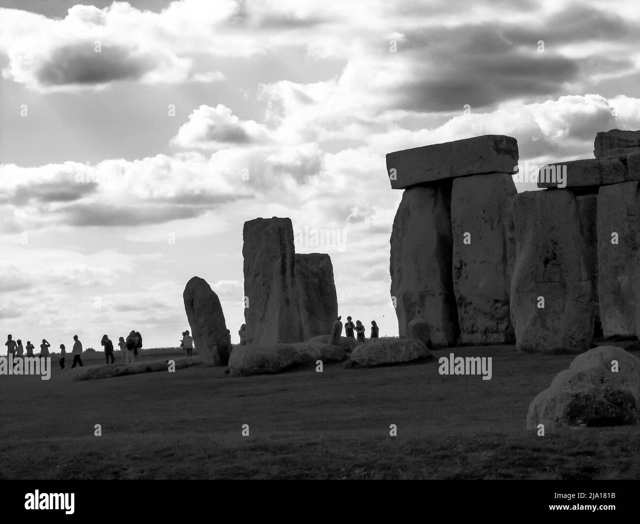 Part of Stonehenge with the silhouettes of tourists in the background, in Black and white giving the scene an ominous feeling Stock Photo