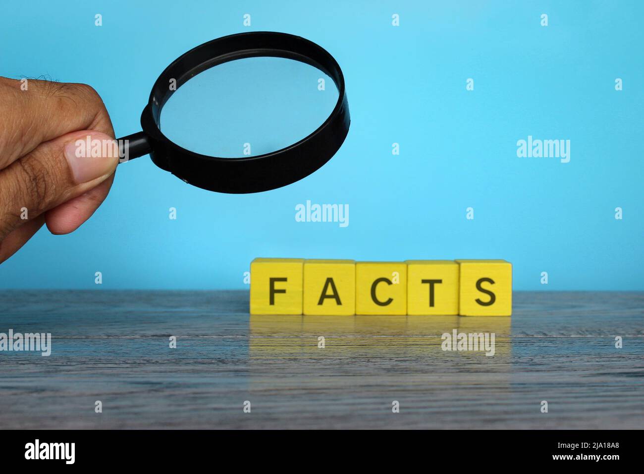 Hand holding magnifying glass and wooden cubes with text FACTS. Checking facts and data concept Stock Photo