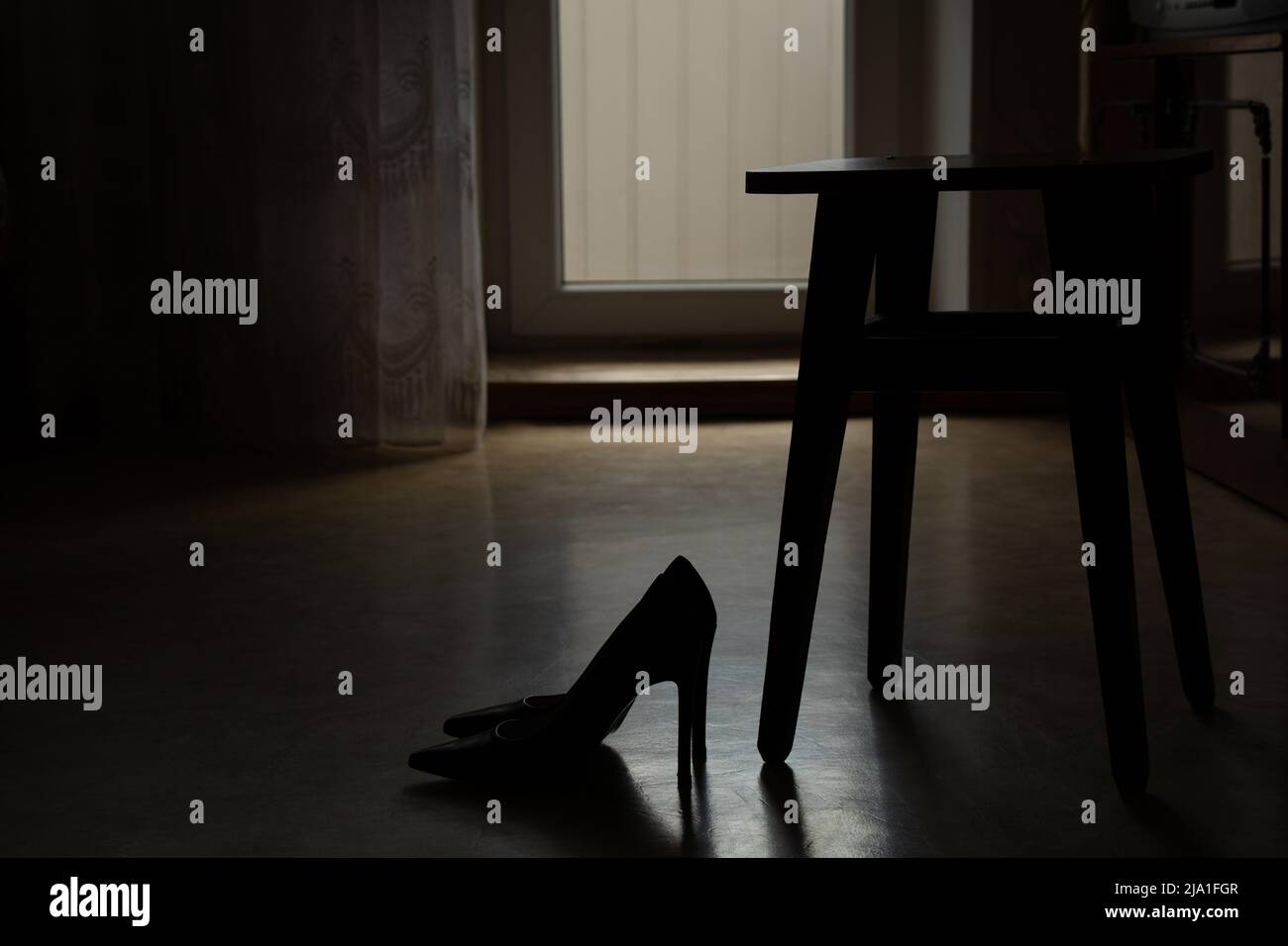 Women's high-heeled shoes stand on the floor of the house near a wooden chair in the dark, fashionable women's shoes, shoes with heels Stock Photo