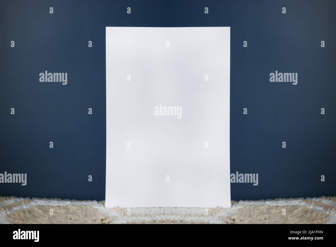 A white sheet of paper stands vertically on a light carpet and an isolated dark background Stock Photo
