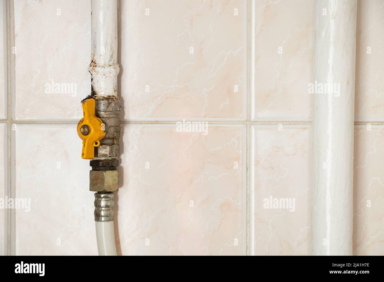 A gas pipe with a faucet against the background of a tile at home in an apartment, a faucet on a pulp pipe in the kitchen Stock Photo