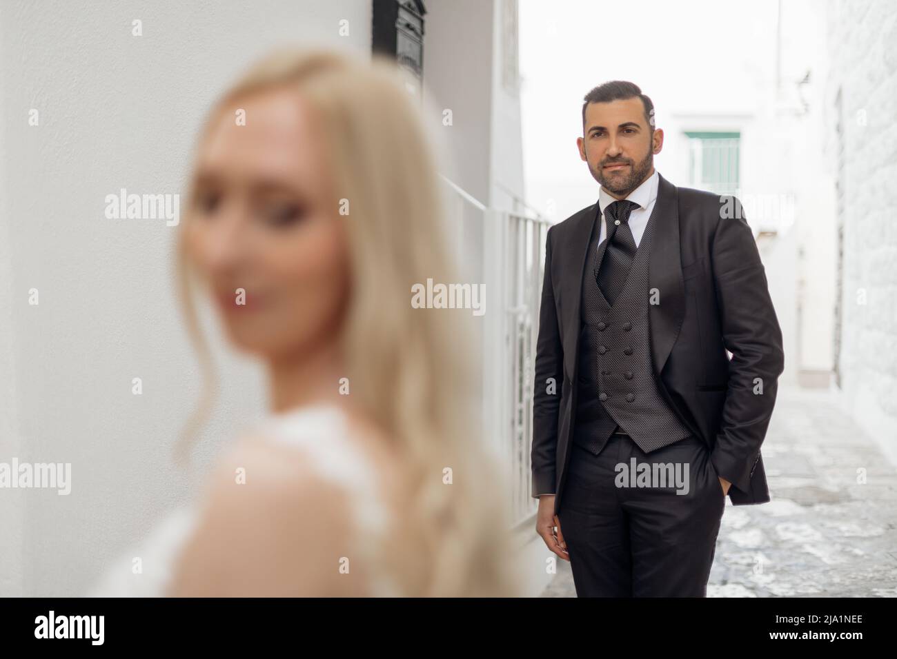 Closeup portrait blurred bride in foreground and handsome groom look at female with love and tenderness. Trendy clothes Stock Photo