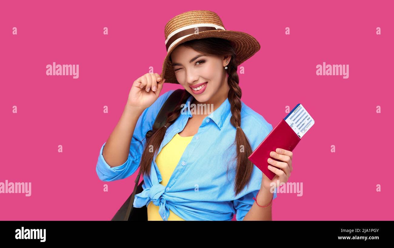 Smiling woman traveler in straw hat and backpack holding passport with plane ticket over pink isolate background Stock Photo