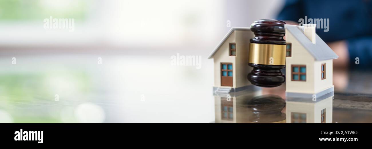 Close-up Of A Judge Striking Gavel Between Split House Over Wooden Desk Stock Photo