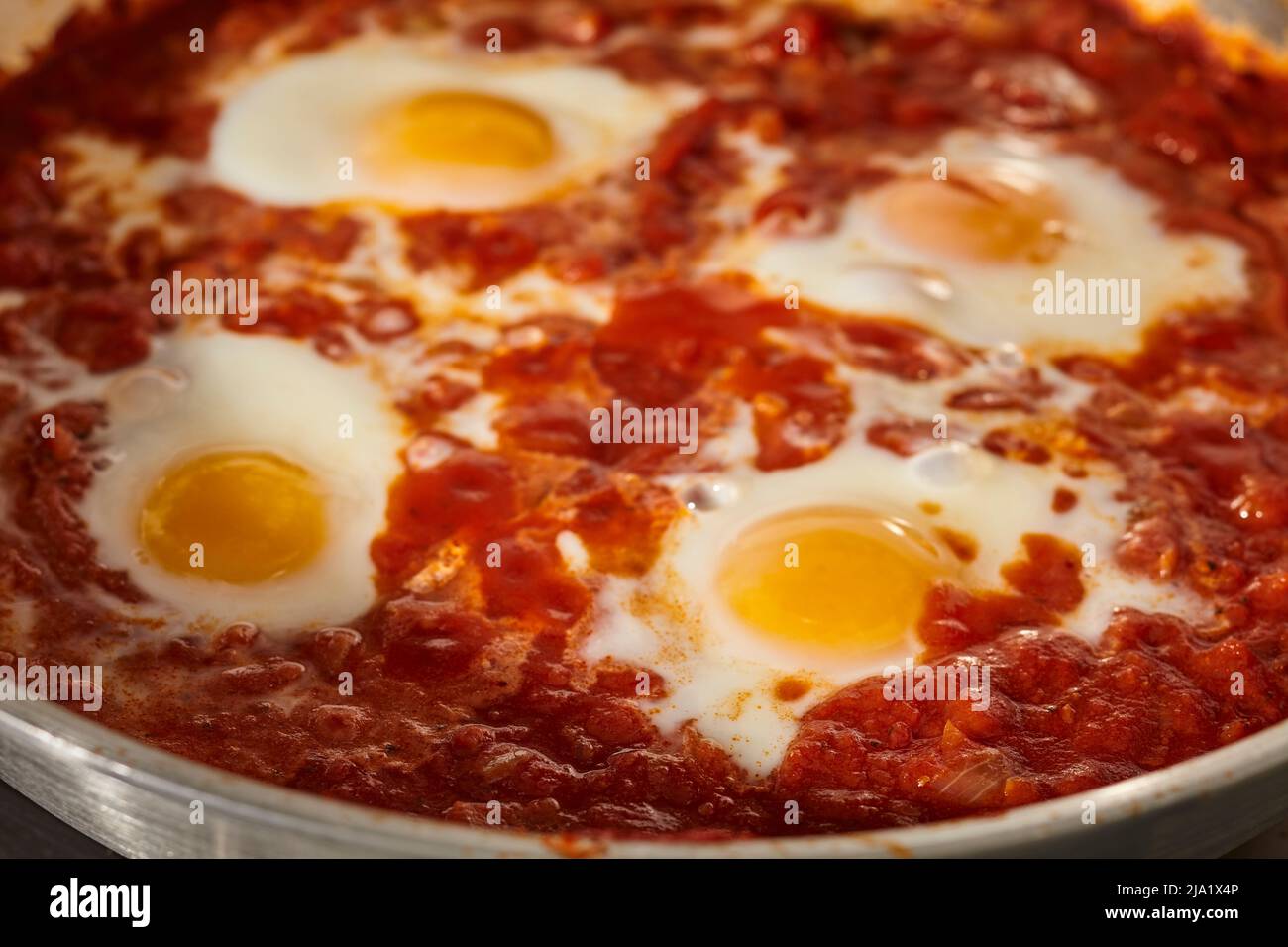 Shakshuka, the Israeli egg and tomato sauce dish, cooking in a steel skillet. Stock Photo