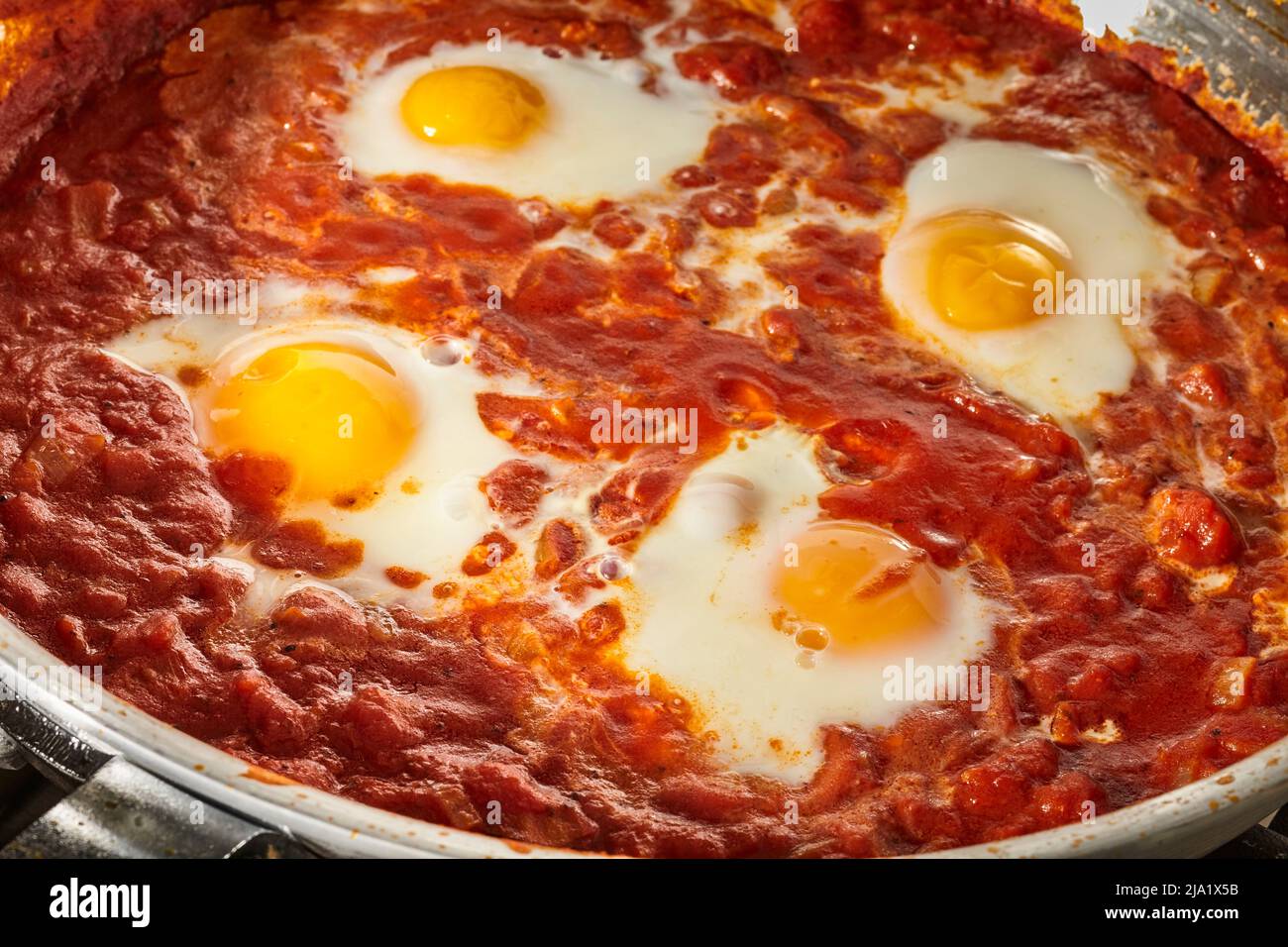 Shakshuka, the Israeli egg and tomato sauce dish, cooking in a steel skillet. Stock Photo