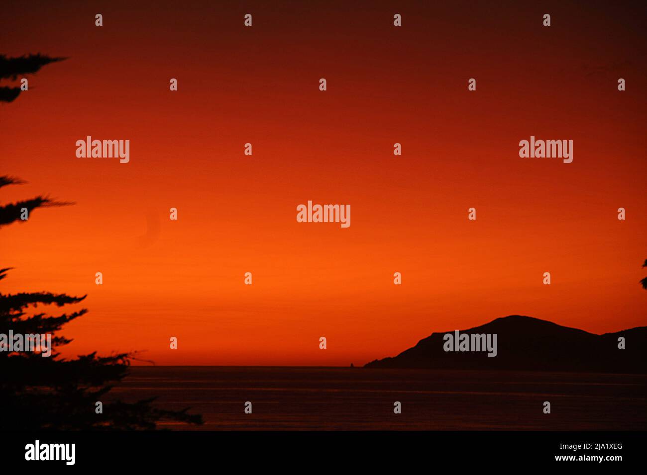 Fiery red sunset silouetting trees and island Stock Photo - Alamy