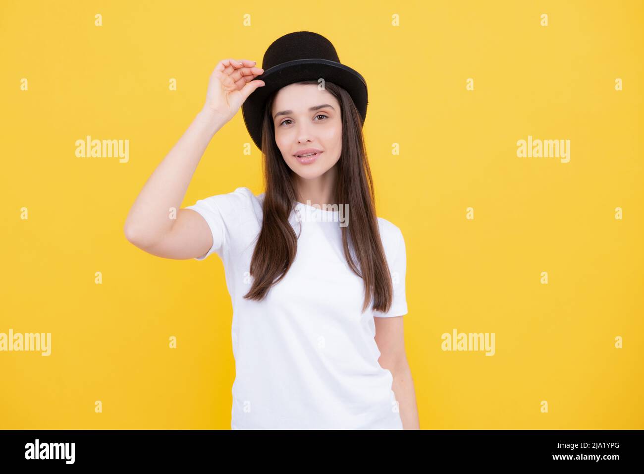 Woman in magician top hat, black vintage cylinder cap on yellow background. Girl circus performer with headwear for magic tricks. Stock Photo
