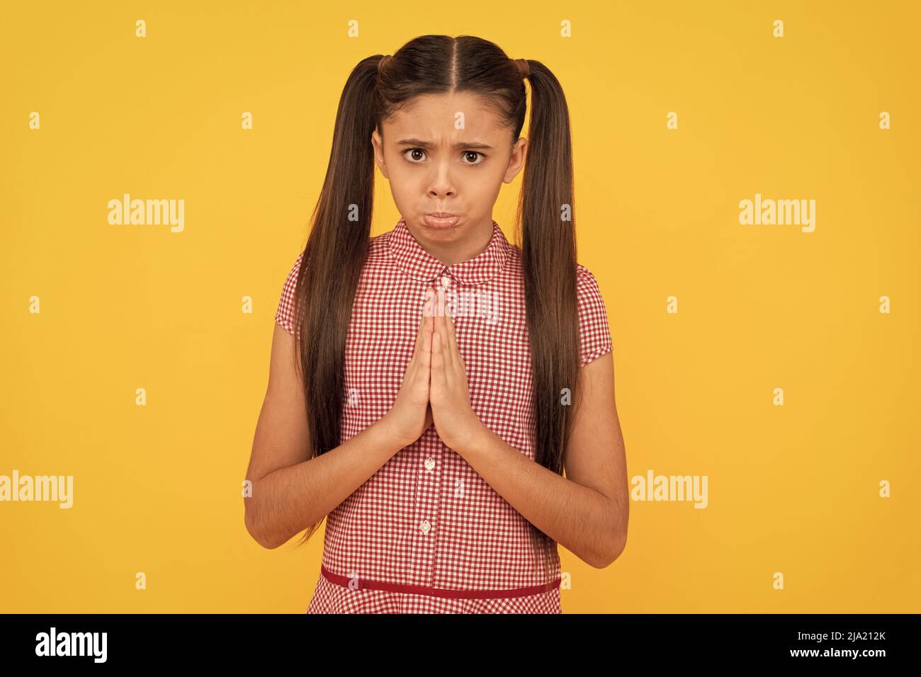 Unhappy girl prayer plead holding palms together in prayer gesture yellow background, pleading Stock Photo