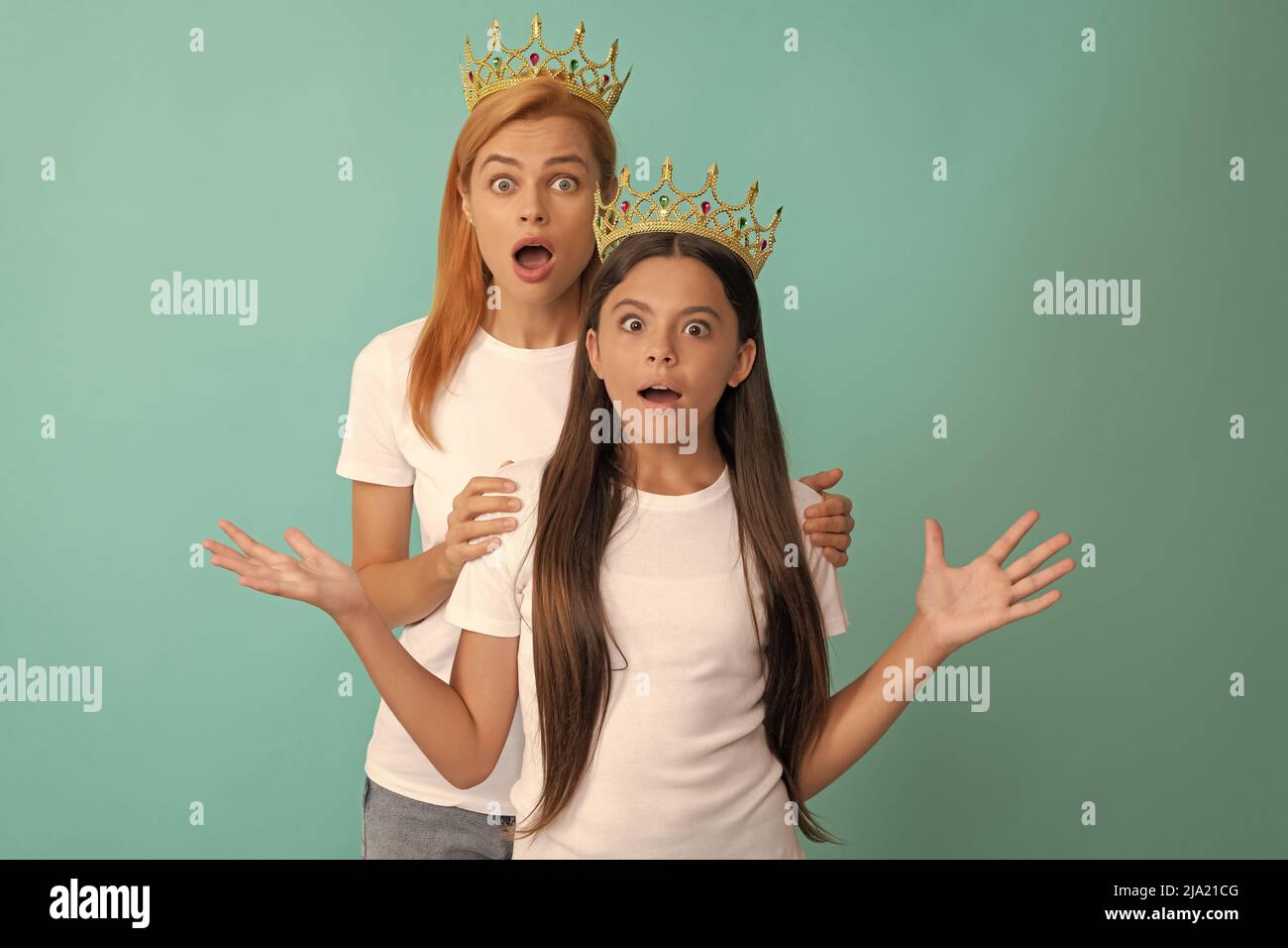 Surprised wide-eyed selfish woman and girl child wear crowns blue background, shock Stock Photo