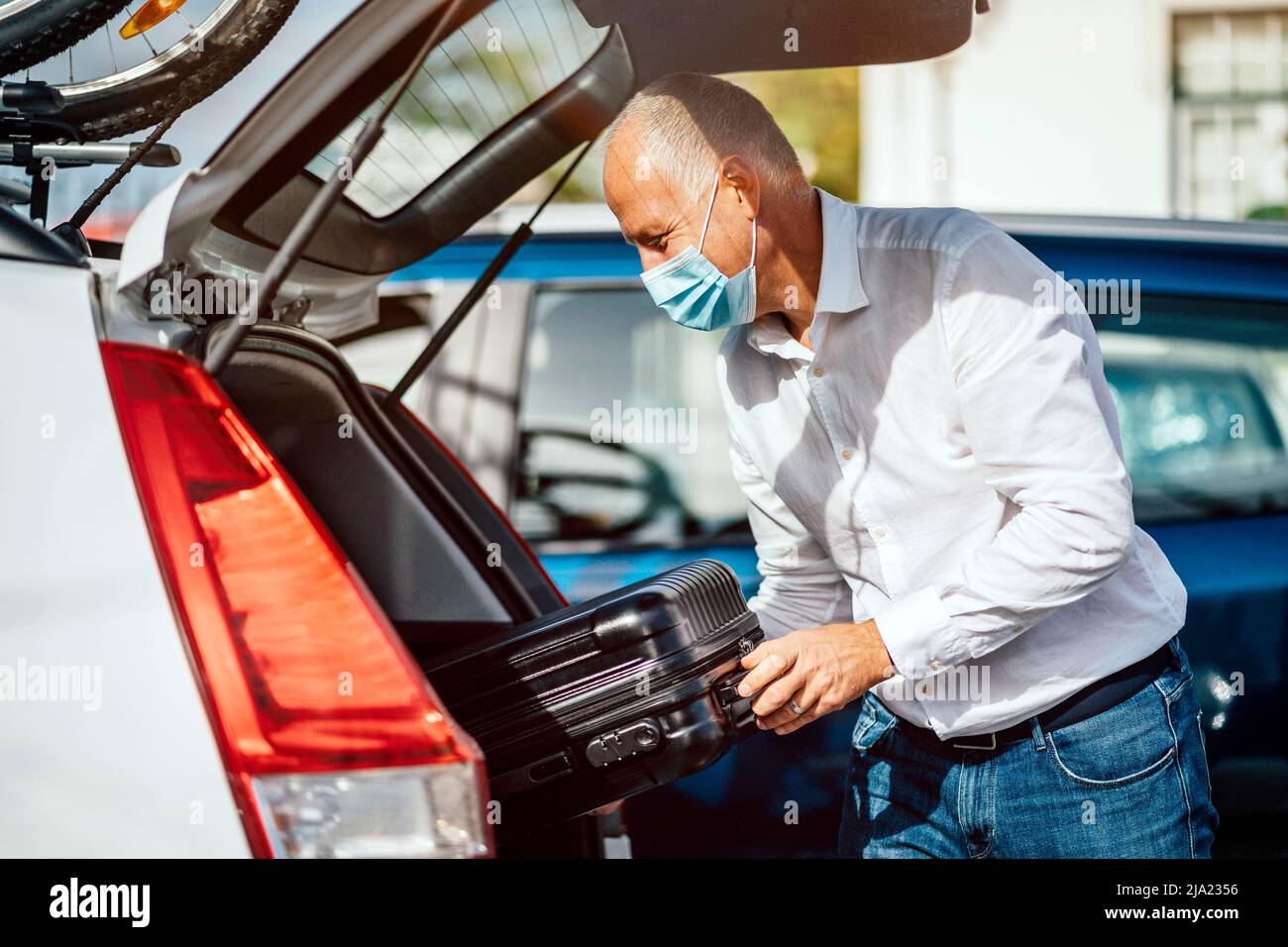 A taxi or Uber driver in mask puts the luggage into the trunk of his car Stock Photo