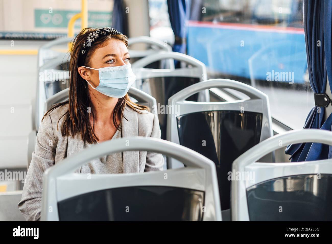 A young woman wearing protective mask looking through the bus window ...