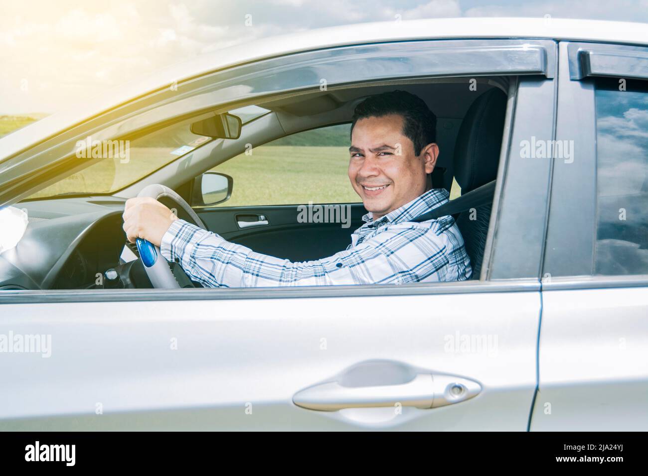 Man smiling at the camera in his car, man smiling happily in his car, image of a person smiling and happy driving a car and looking at the camera Stock Photo