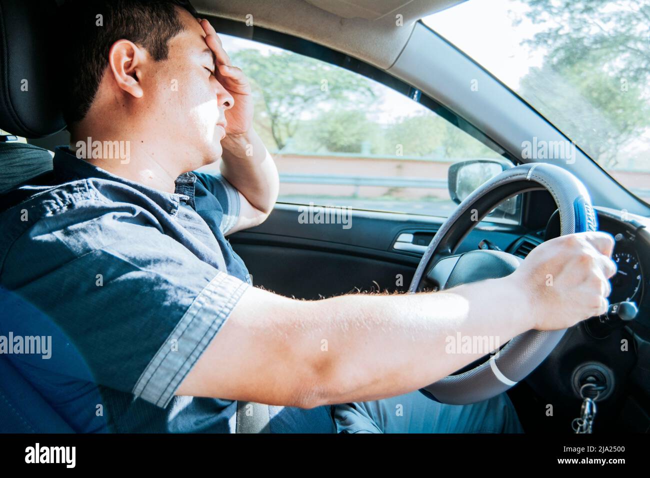 Fatigued driver stuck in traffic, concept of a fatigued man in his car, stressed. A driver with a headache in traffic, A person with a headache in Stock Photo
