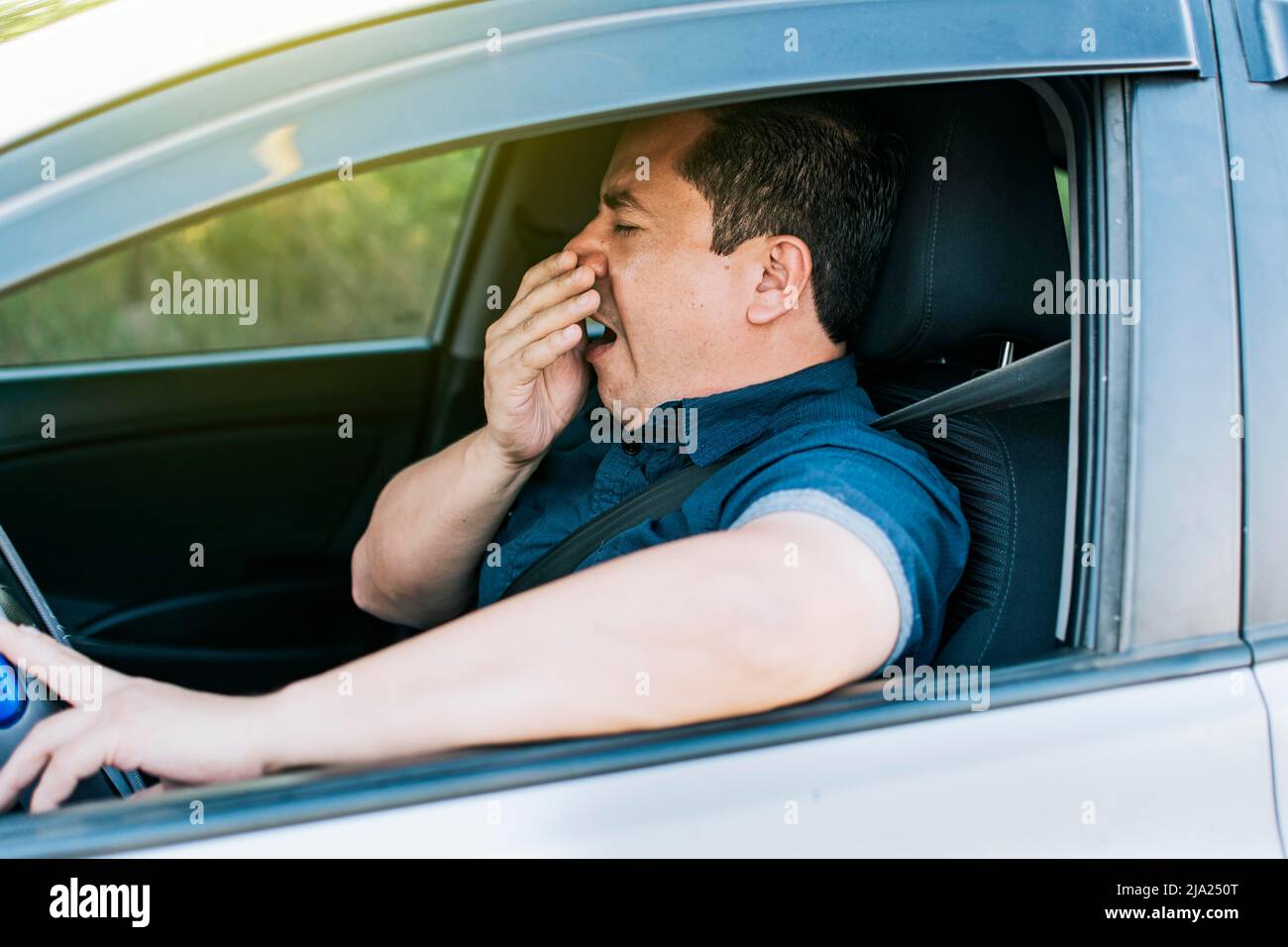 Tired driver yawning, concept of man yawning while driving. A sleepy driver at the wheel, a tired person while driving Stock Photo