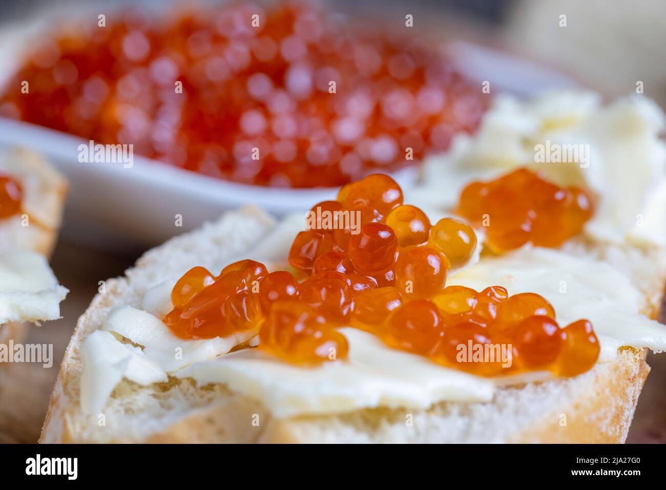 red salmon or trout caviar with white baguette and butter, making ...
