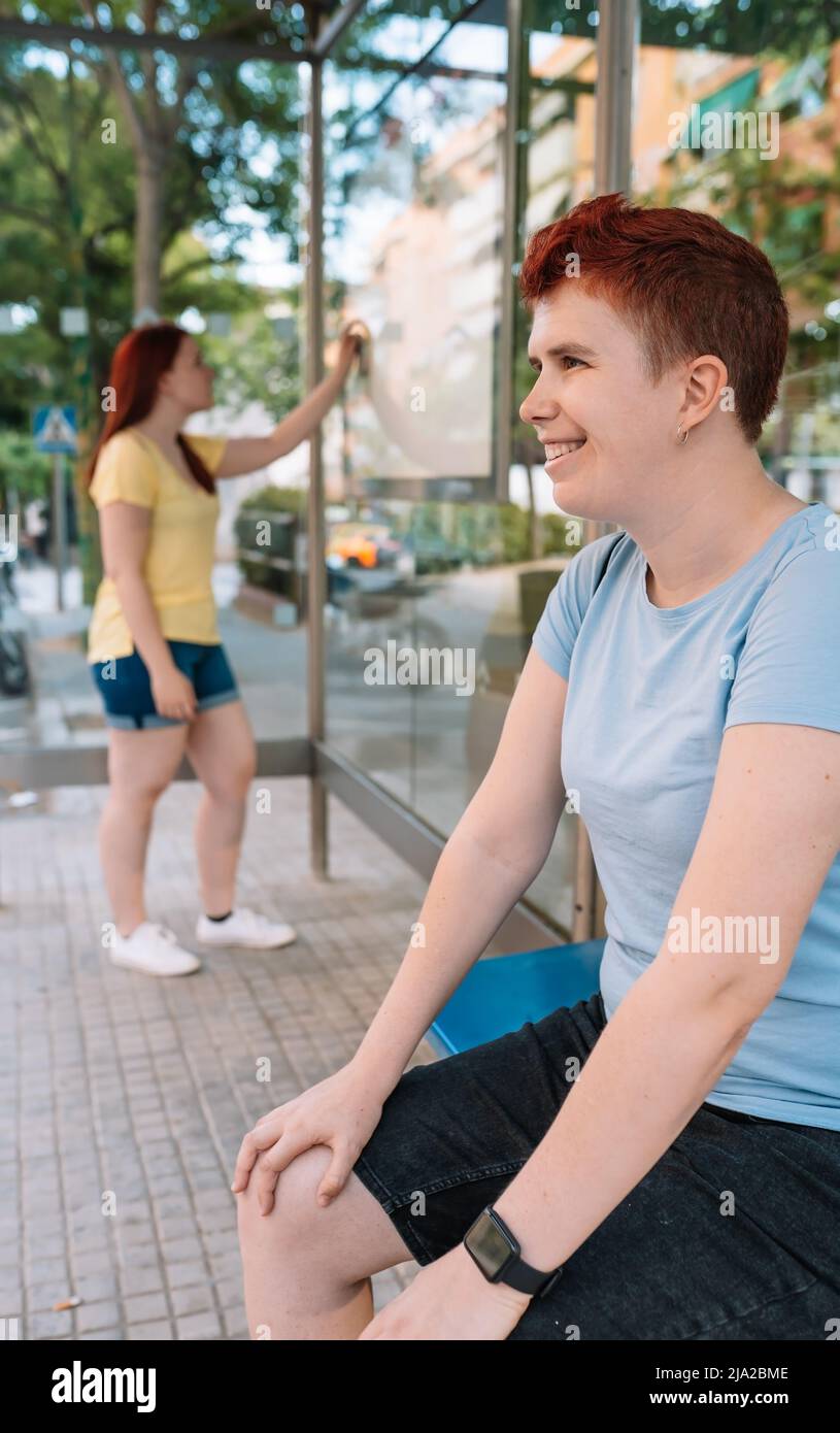 young girl sitting, waiting at the bus station in the big city. woman outdoors at the bus stop while waiting for the tram. vertical. Stock Photo