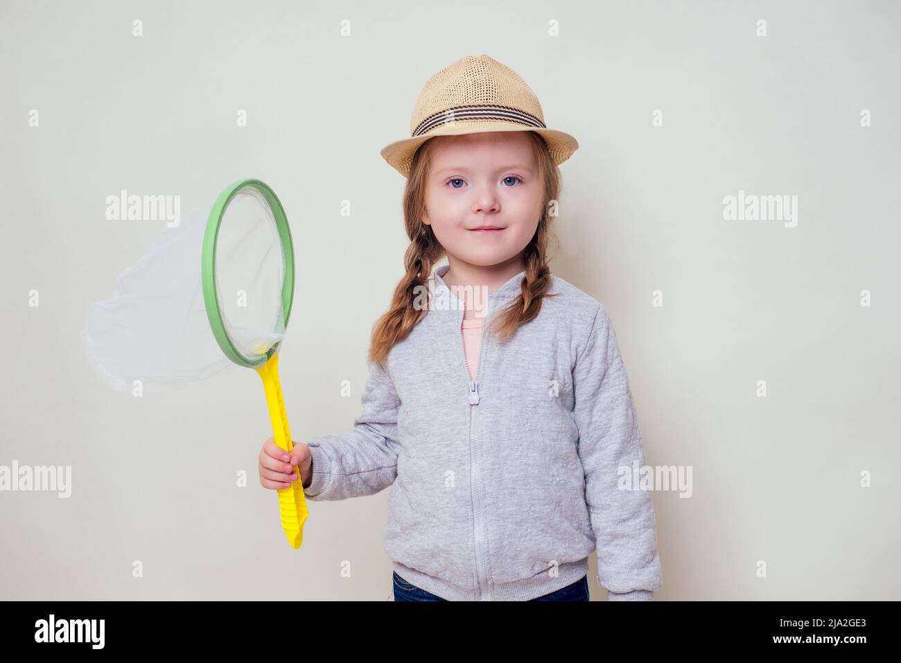 little and beautiful blonde girl in a straw hat holds a butterfly net in her hand and catches butterflies studio white background.Cheerful female kid Stock Photo