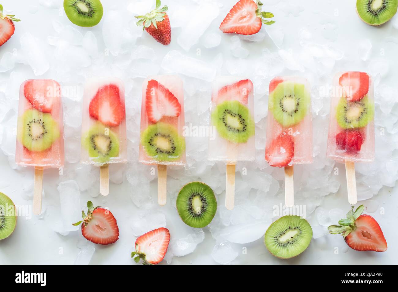 Strawberry kiwi popsicles on ice surrounded by slices of strawberries and kiwi. Stock Photo
