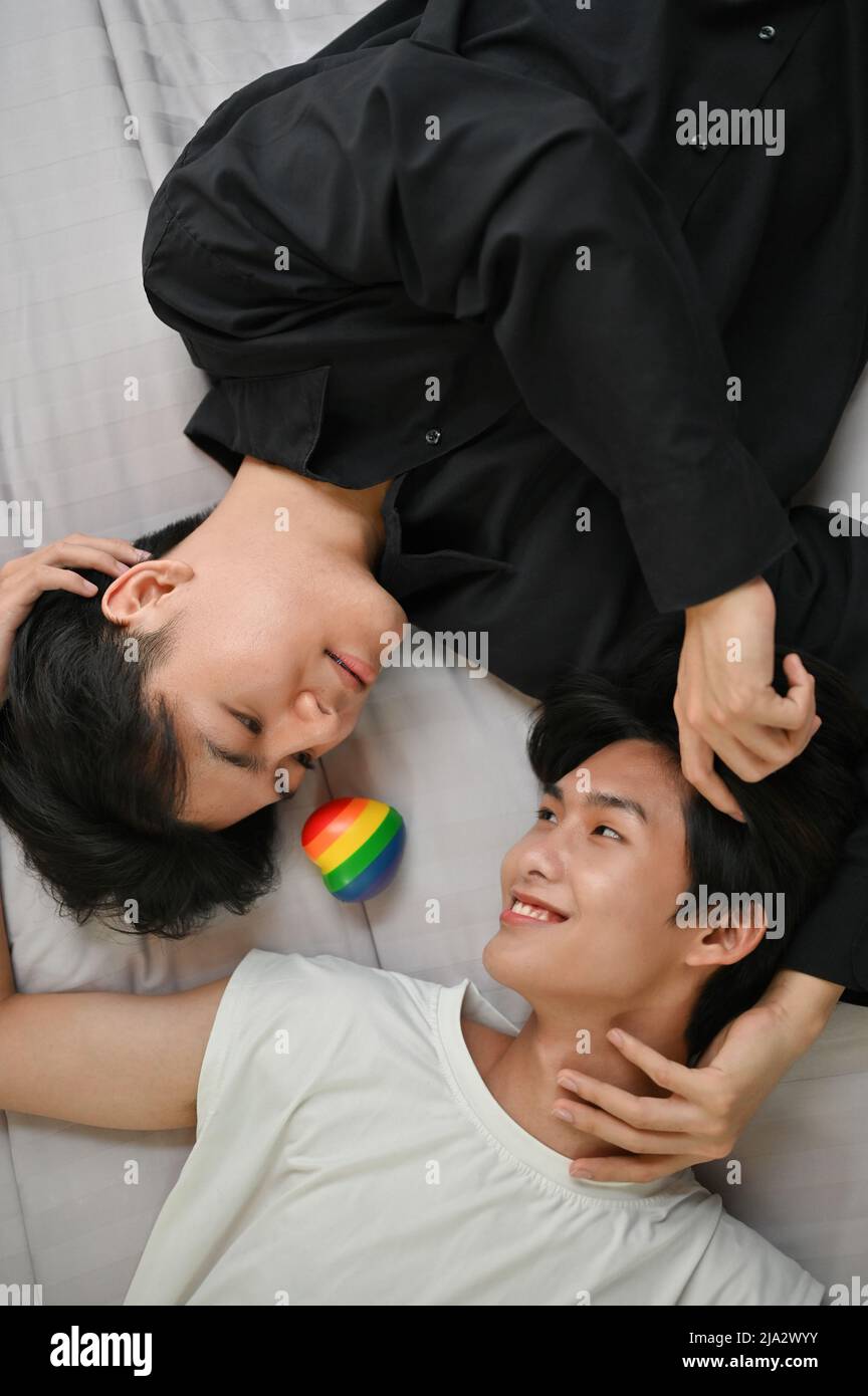 Portrait of attractive asian young gay men couples laying on bed together, touching face with romantic feeling, showing some LGBT lover affection. Asi Stock Photo