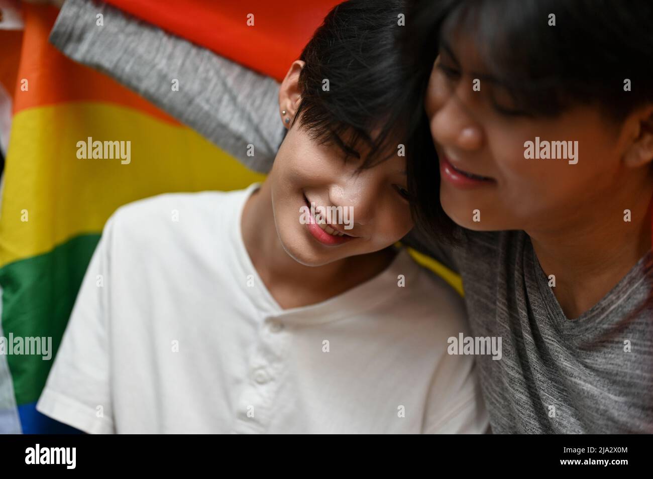 Beautiful Asian young gay man in a warm embrace of his gay boyfriend and LGBT flag. Cuddling or hugging. young LGBT couples. Stock Photo