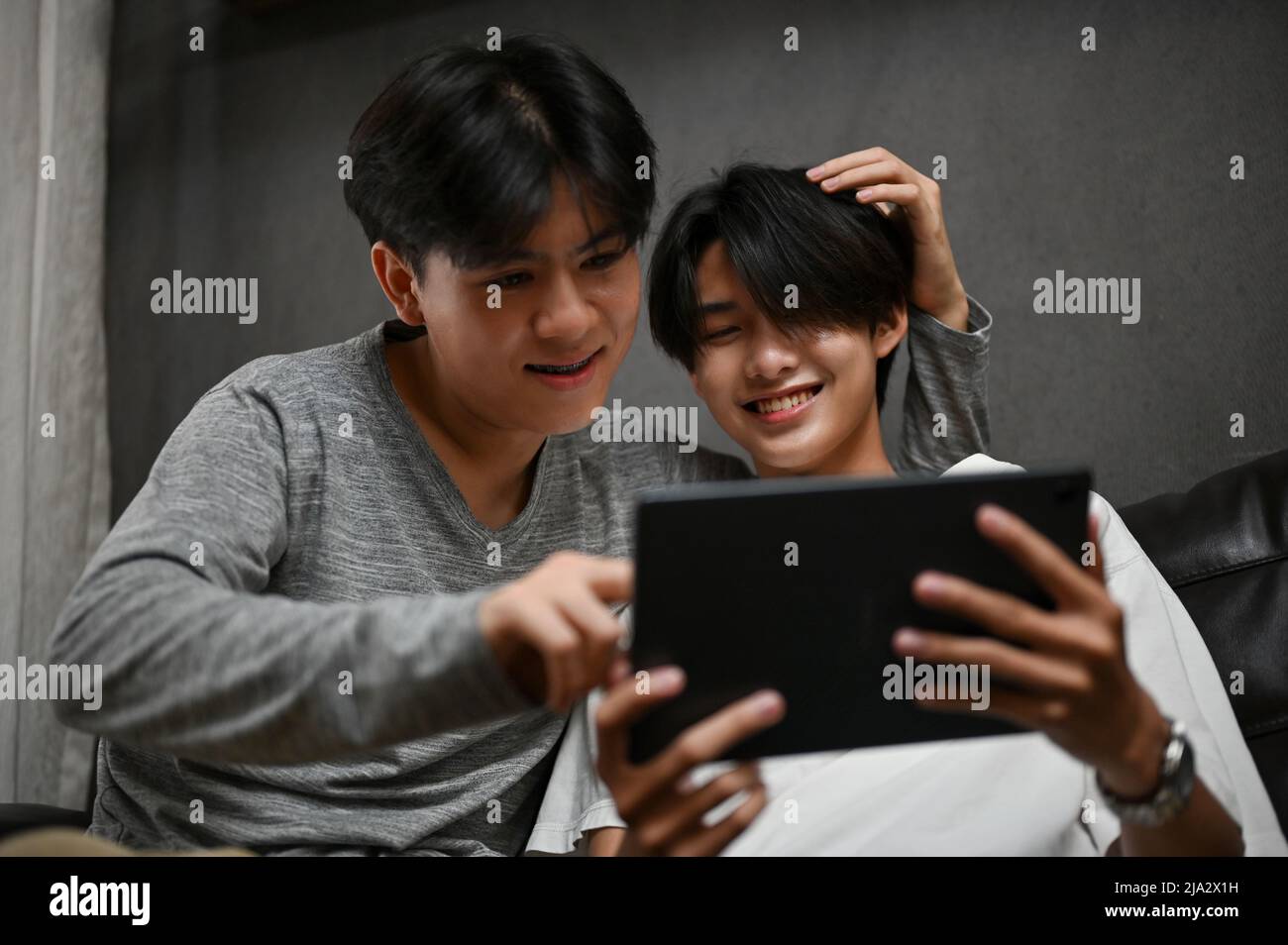 Two Asian teens gay men boyfriends spending time together, enjoy watching something on tablet in living room. LGBT couple's activities concept Stock Photo