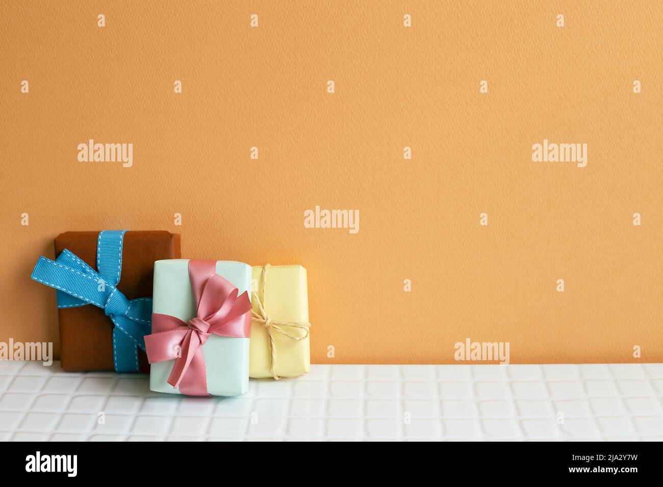 Colorful gift boxes on white table. orange wall background. copy space Stock Photo