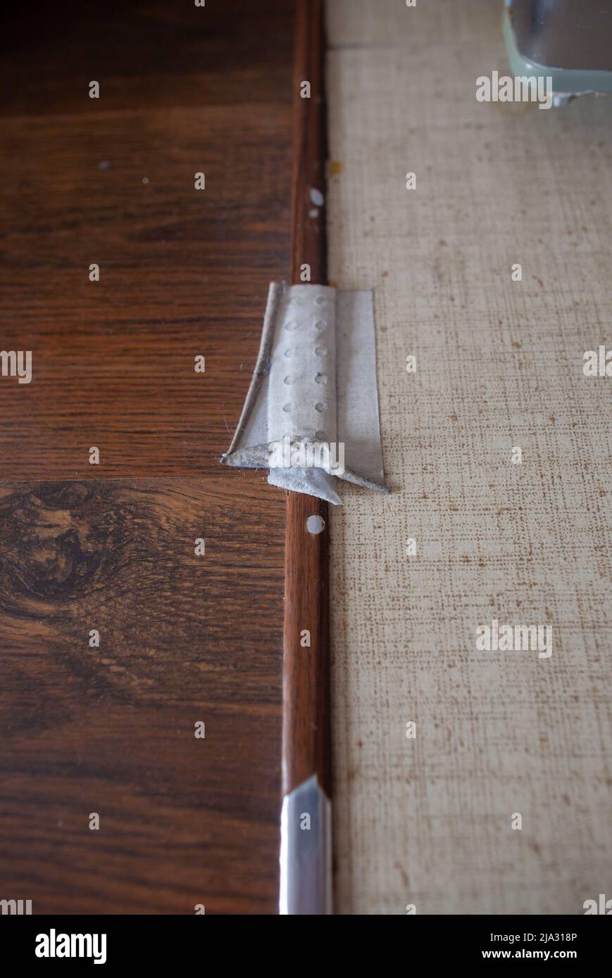 Closeup of damaged metal board separating wooden and tiles floor with plaster covering sharp fragment Household protection concept Stock Photo