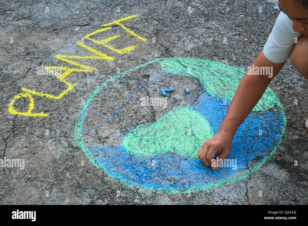 Young woman drawing with colorful chalk on asphalt.  Asian woman paints a beautiful world with the message Planet on courtyard. Concept of world envir Stock Photo