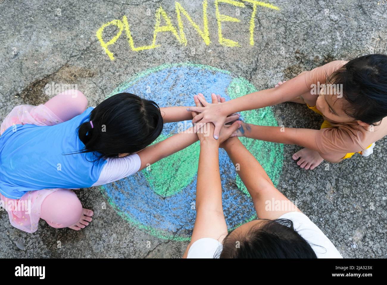 Volunteer family paints a beautiful world with the message Planet on asphalt and put hands together. Concepts of world environment day and peace day. Stock Photo
