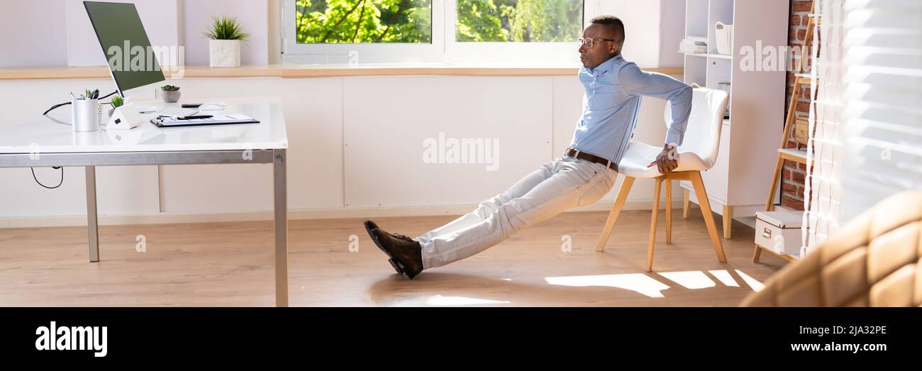 Side View Of A Young Man Doing Stretching Exercise In Office Stock Photo