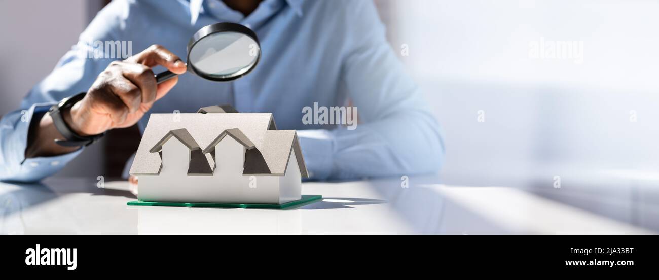 Human Hand Holding Magnifying Glass Looking House Model Over White Desk Stock Photo
