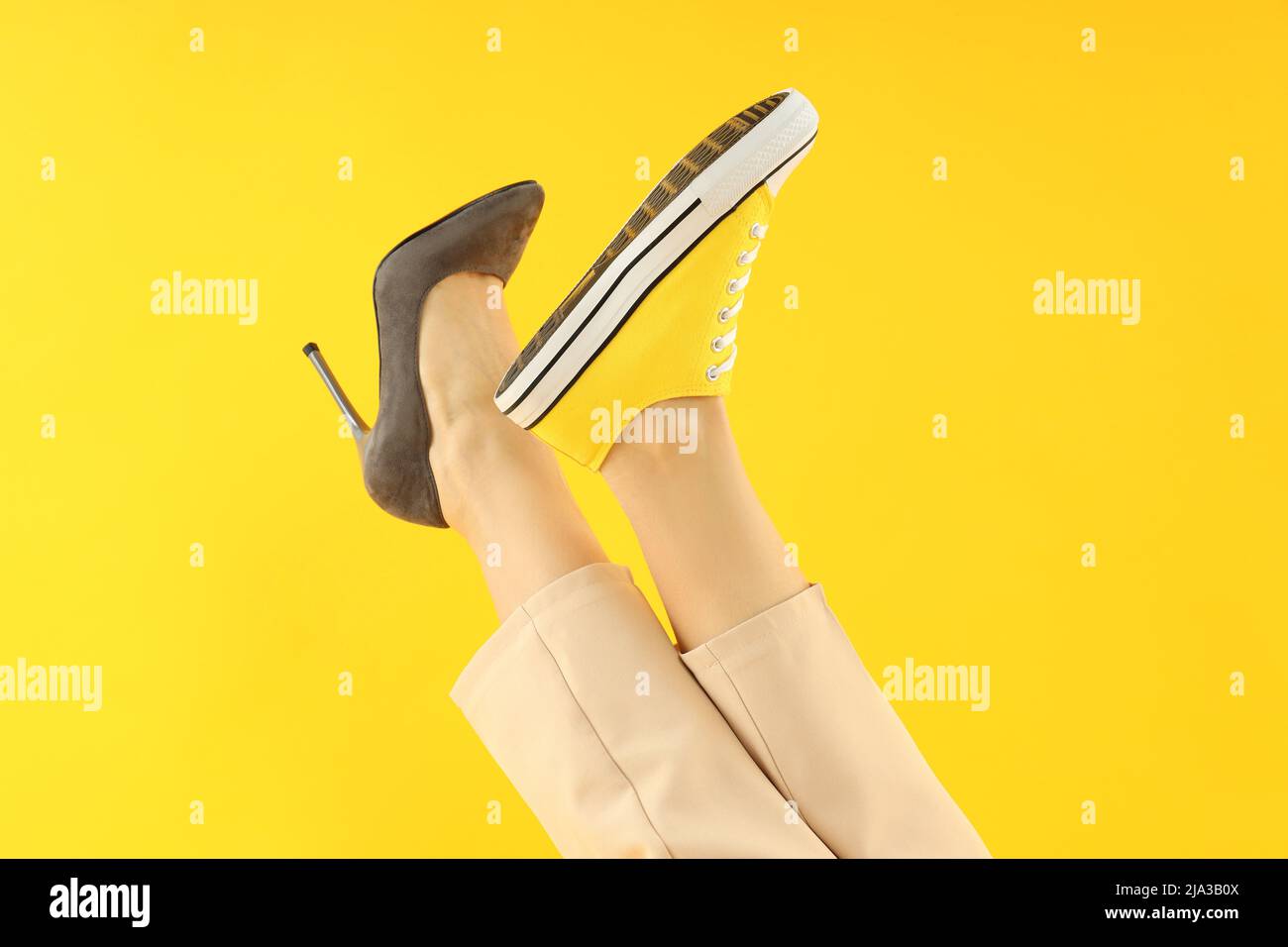 Female legs in heel and sneaker on yellow background Stock Photo