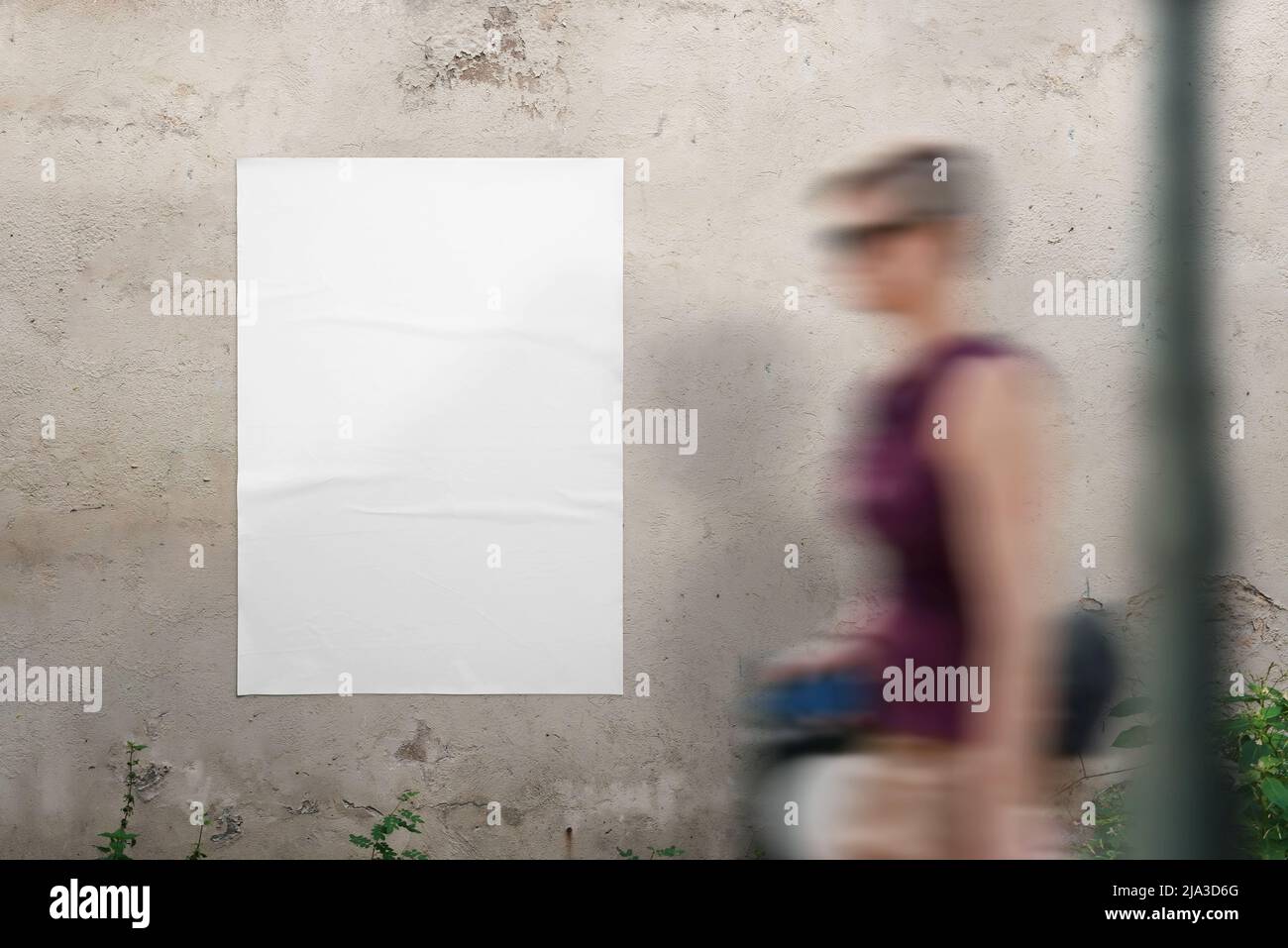 Blank poster mockup on the wall for design presentation. A young woman walks past Stock Photo