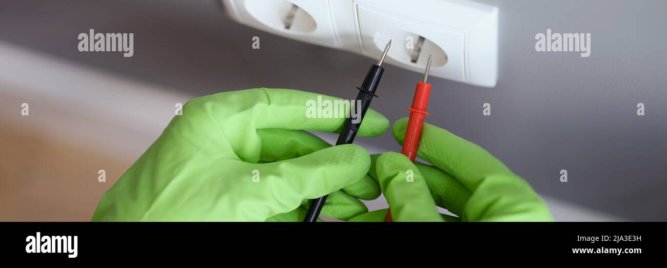 Measuring voltage with a multimeter, hands in rubber gloves Stock Photo