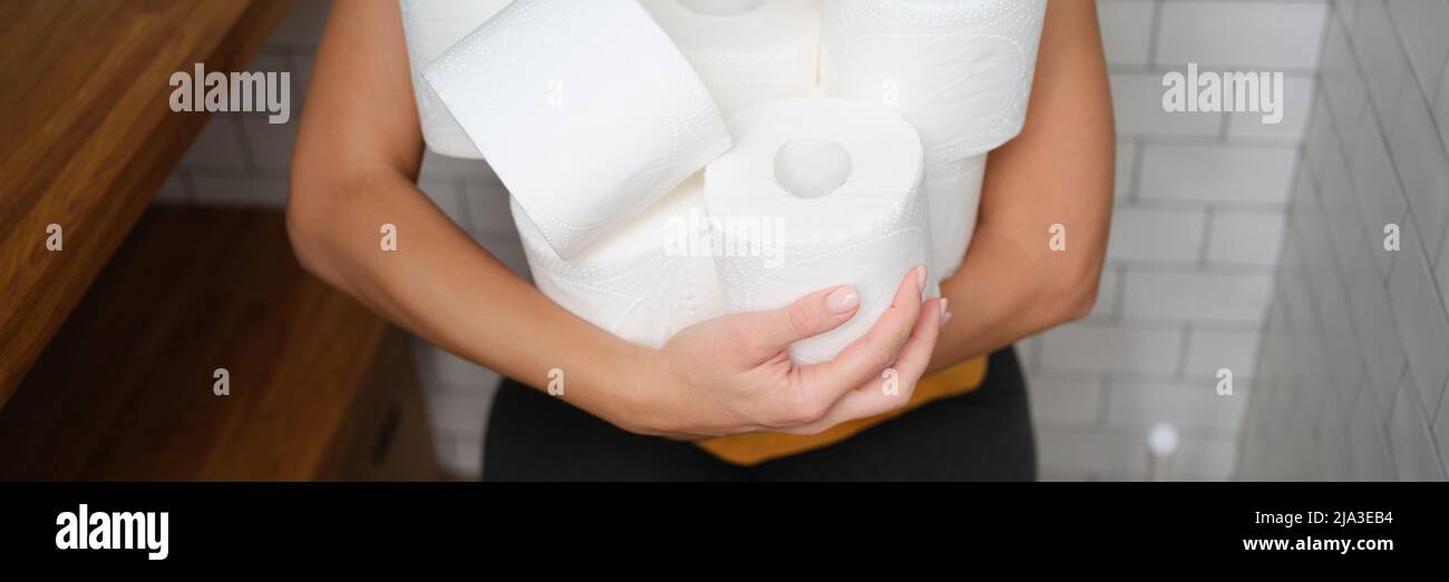 Woman sitting on toilet with rolls of toilet paper Stock Photo